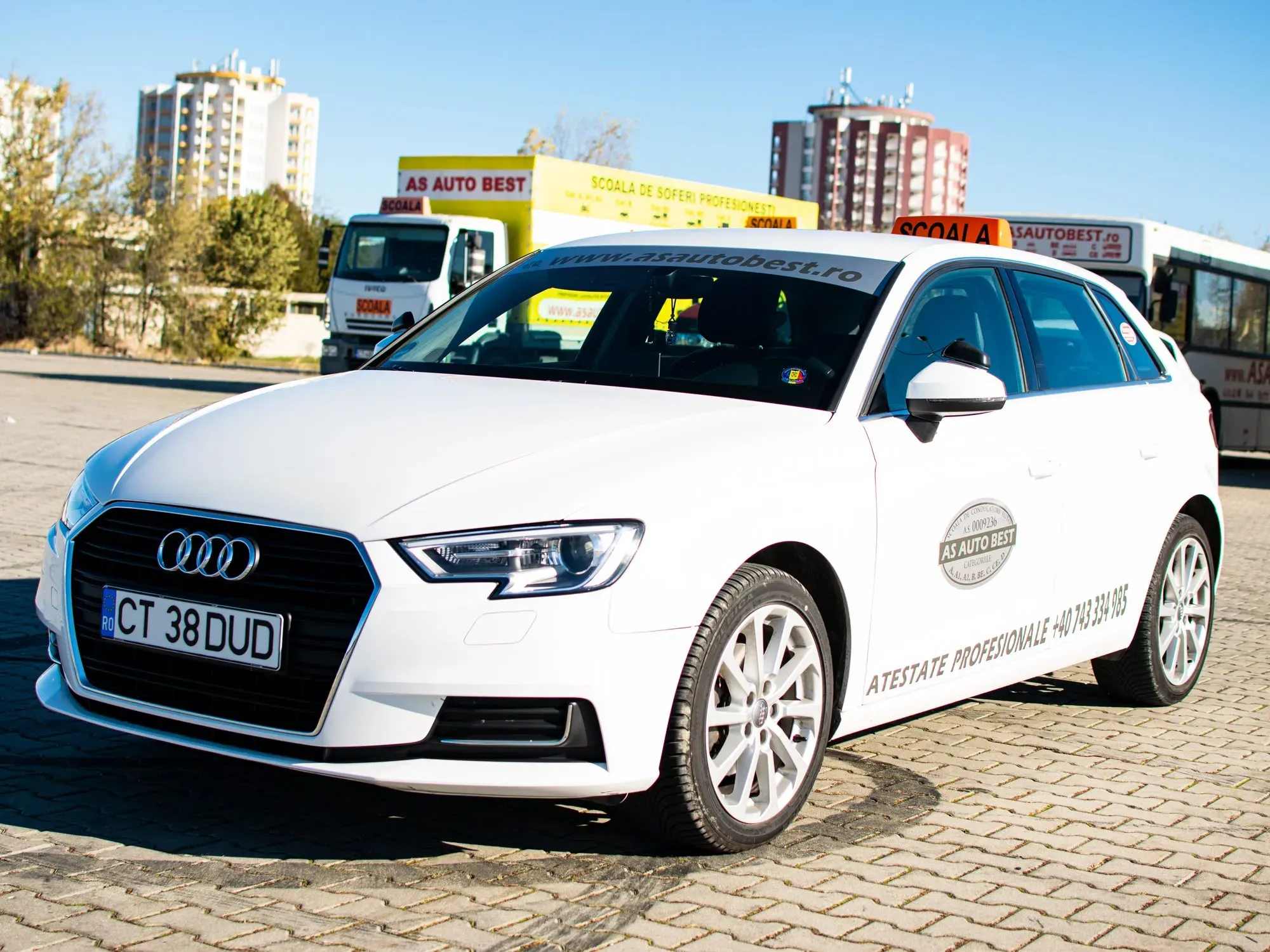 Audi A3 de școală pe poligon, cu camionul și autobuzul școlii în fundal
